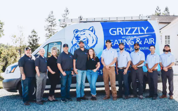 A team of Grizzly Heating and Air employees standing in front of a company van with a blue bear logo