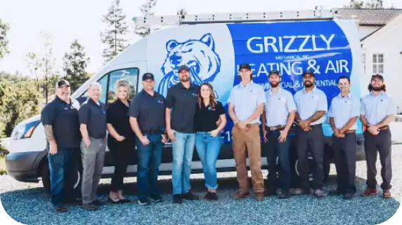 A team of Grizzly Heating and Air employees standing in front of a company van with a blue bear logo