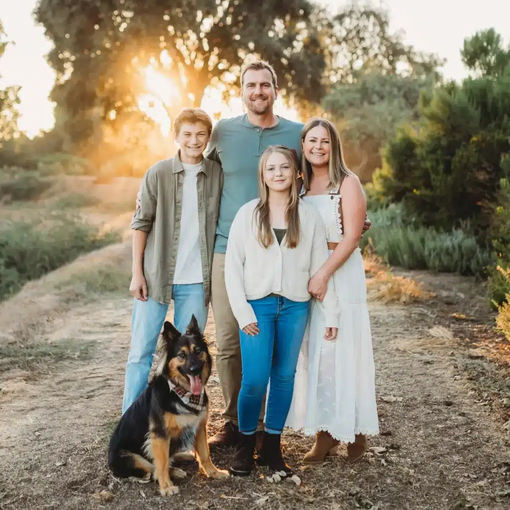 Owner of Grizzly Heating & Air with his family and their dog, smiling outdoors at sunset. Dedicated to providing expert heating and air conditioning services with a family-first approach.